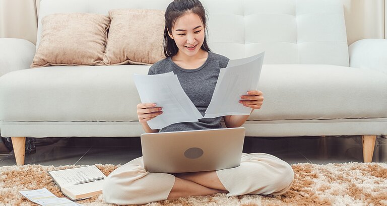 Junge Frau sitzt im Wohnzimmer und überprüft Rechnungen