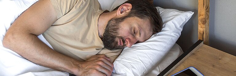 Mann schläft entspannt im Bett.
