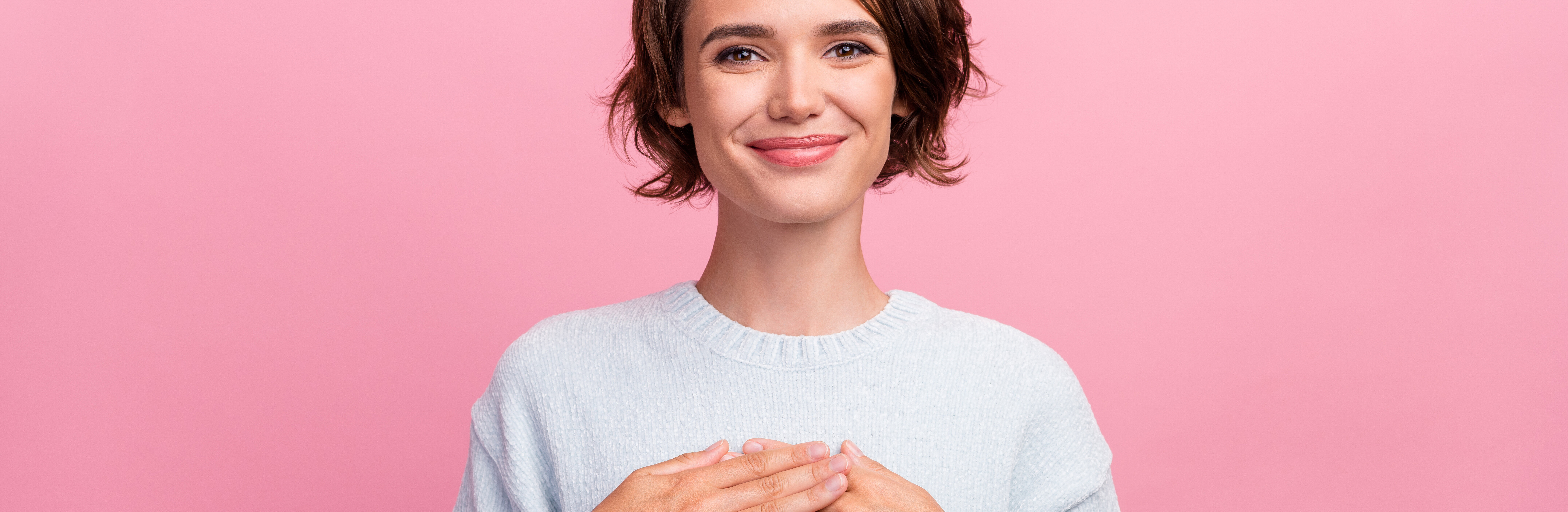 Junge Frau im Pullover legt Hand auf die Brust.