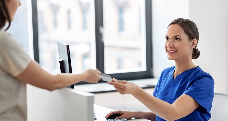 Patient überreicht der Arzthelferin seine Gesundheitskarte