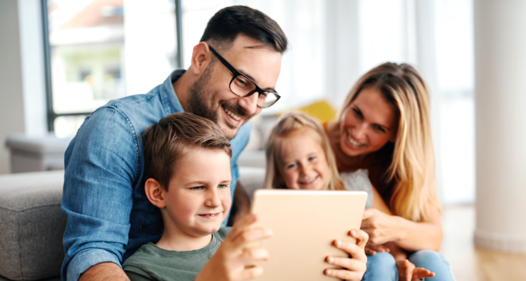 Familie sitzt zusammen auf dem Sofa und schaut aufs Tablet
