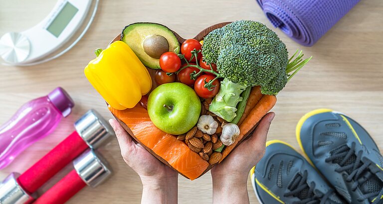 Schale mit gesunden Lebensmitteln sowie Sportausrüstung