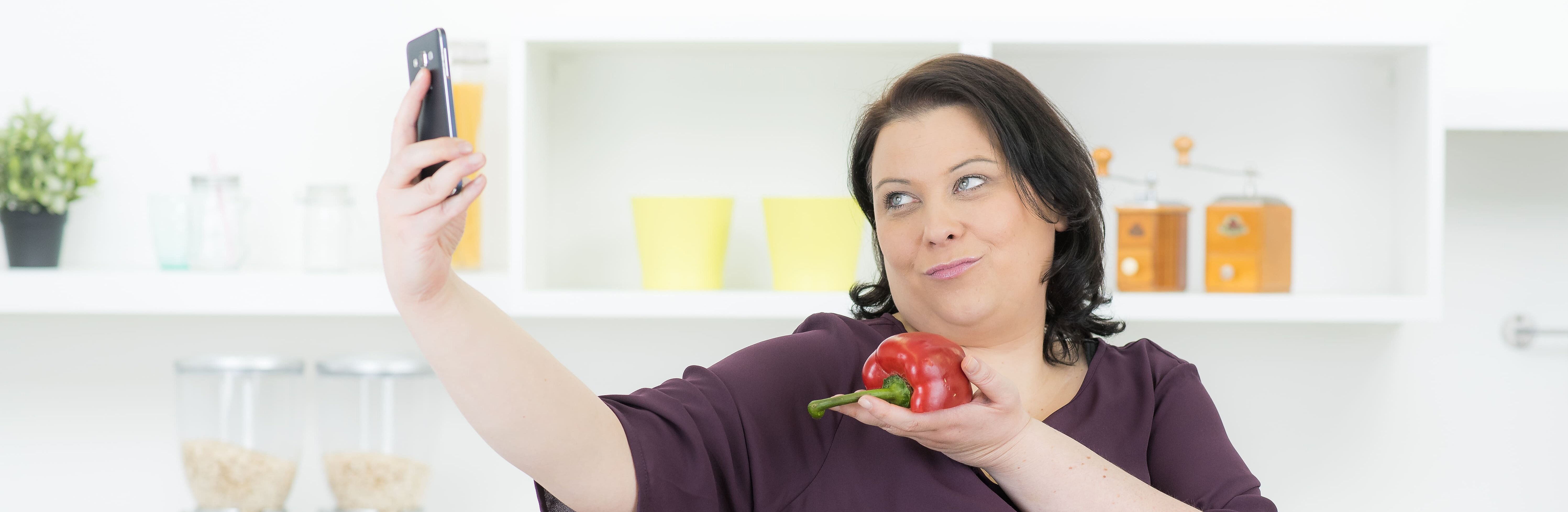 Frau mit runden Körperformen fotografiert sich mit frischer Paprika