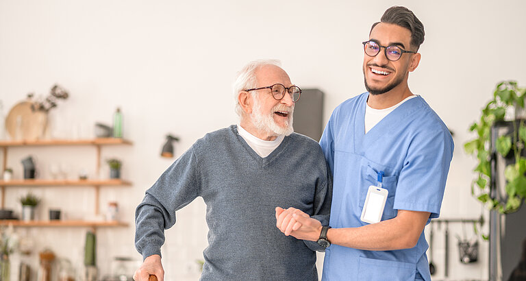 Pfleger und rüstiger Senior gehen durch die Wohnung