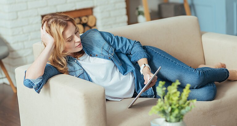 Frau sitzt auf der Couch mit einem Tablet in der Hand