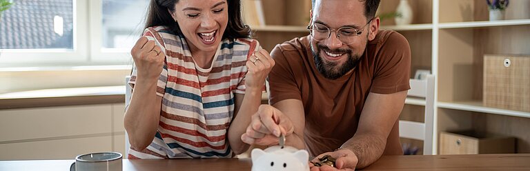 Junges Paar wirft erfreut Geld in Sparschwein.