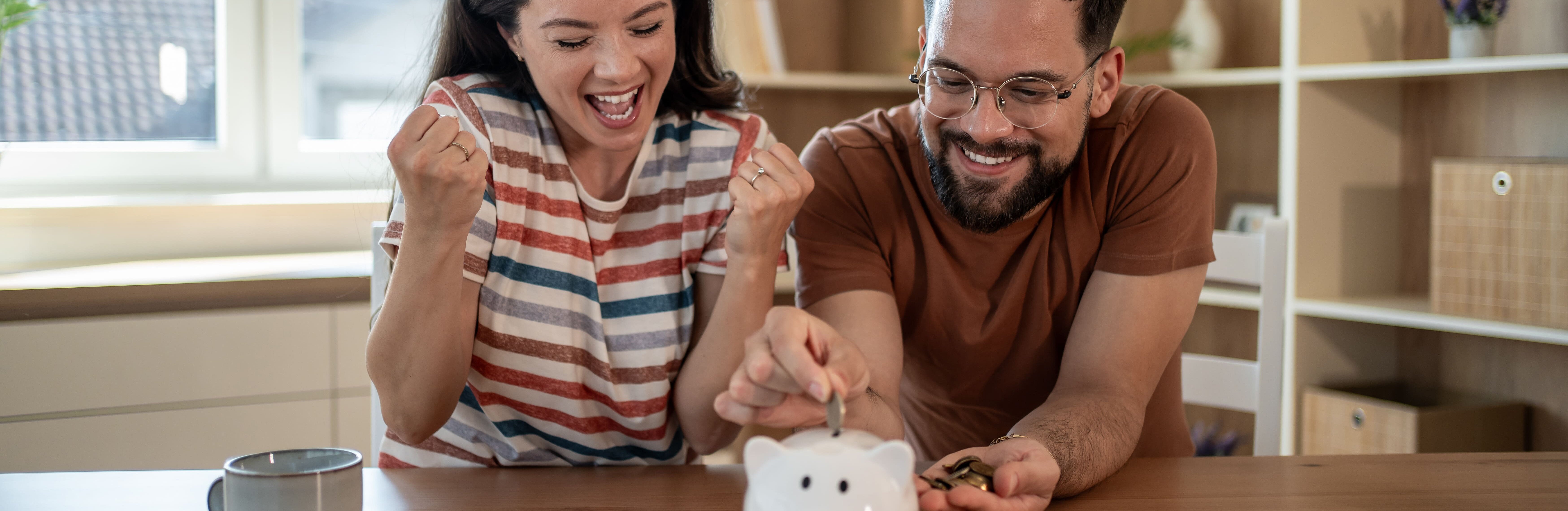 Junges Paar wirft erfreut Geld in ein Sparschwein.