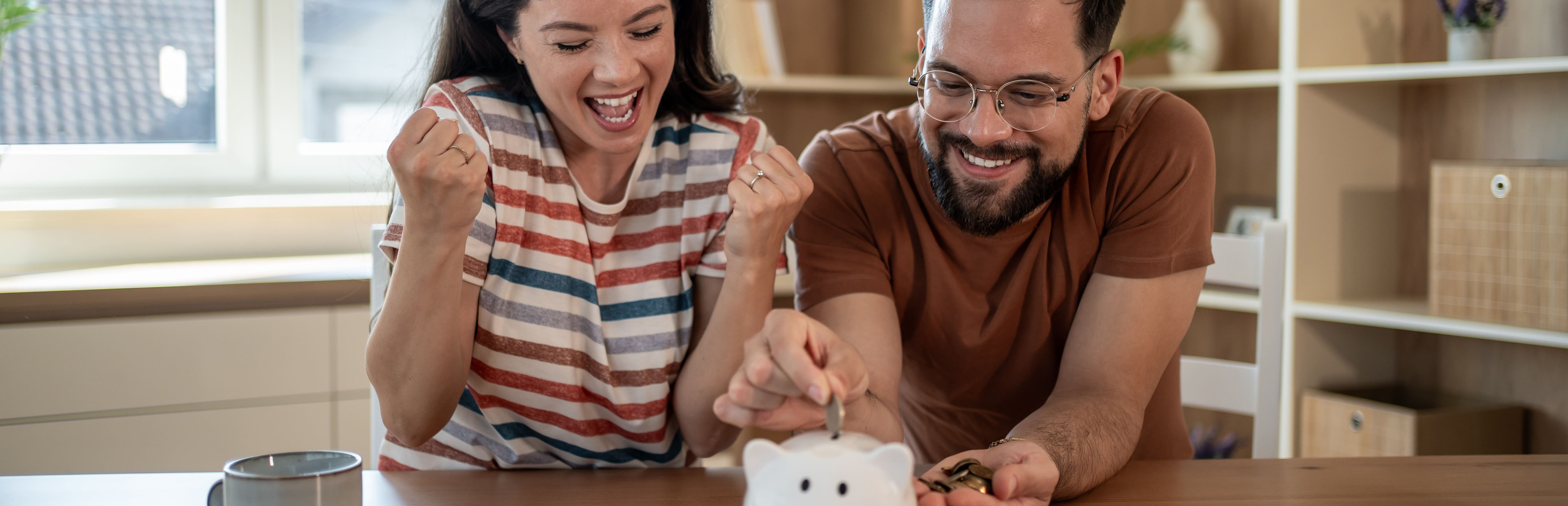 Junges Paar wirft erfreut Geld in Sparschwein.
